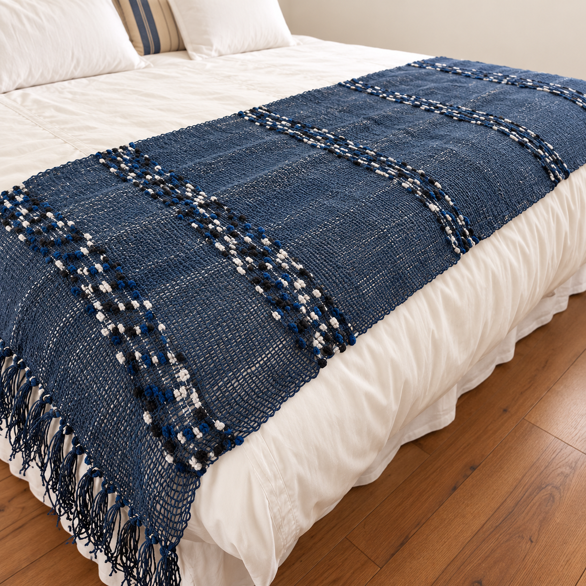 Piecera azul tejida a mano con franjas decorativas sobre ropa de cama blanca